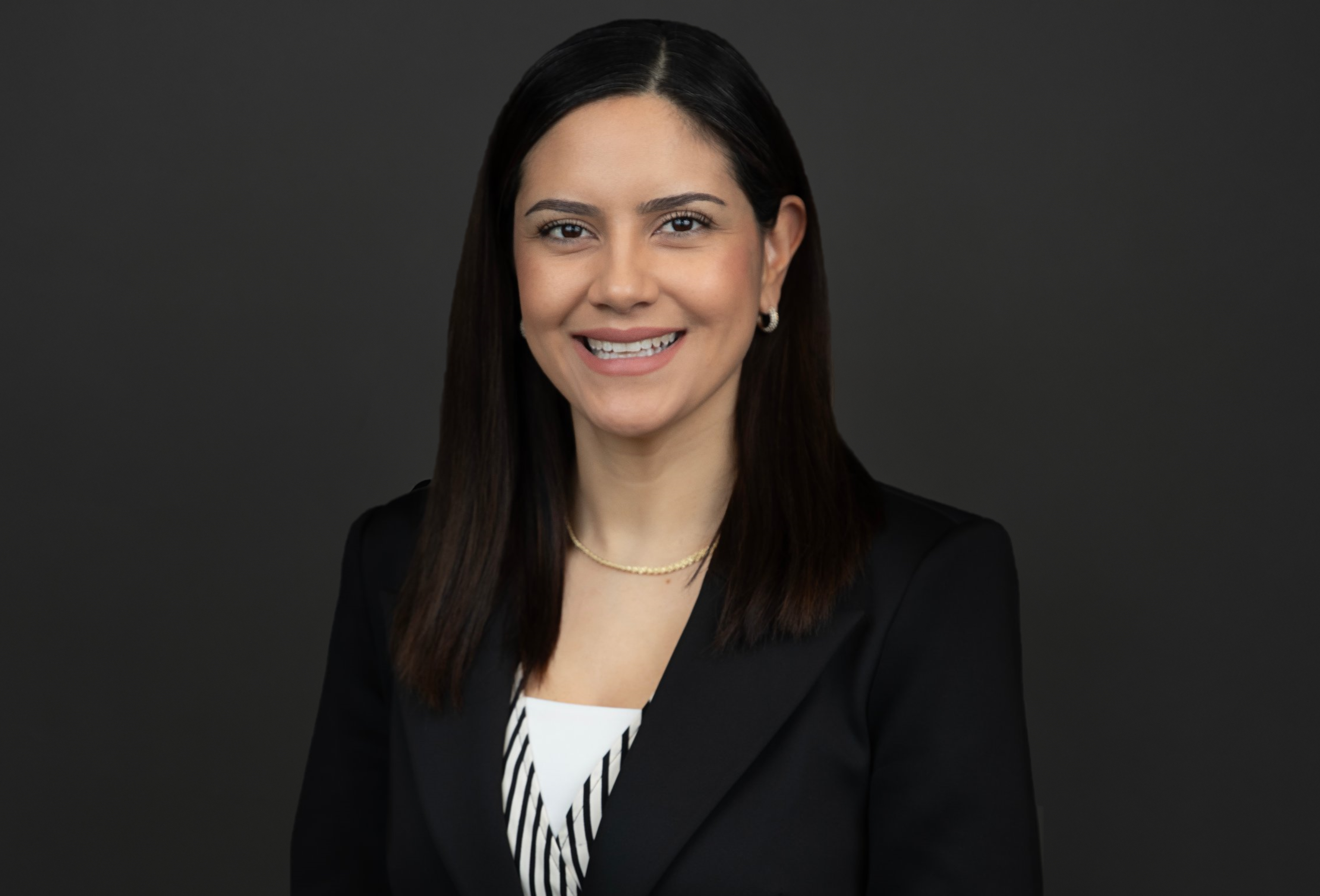 A woman with black hair and a black suit smiling in a h