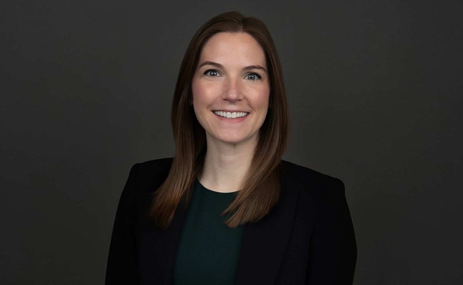 A woman with brown hair and a black suit smiling in a h